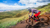 Person riding a mountain bike on a trail with a scenic view of mountains and clouds.